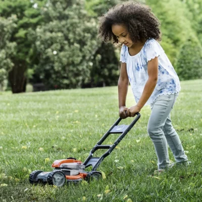 Petite fille qui joue avec jouet tondeuse Husqvarna dans un jardin